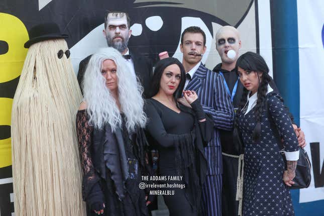 Seven cosplayers dressed as the '90s version of The Addams Family. 